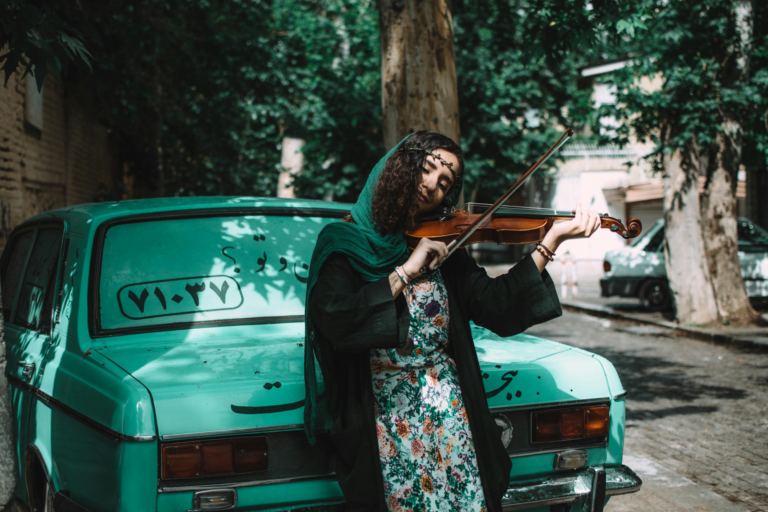 Woman Playing Violin While Leaning On Green Vehicle